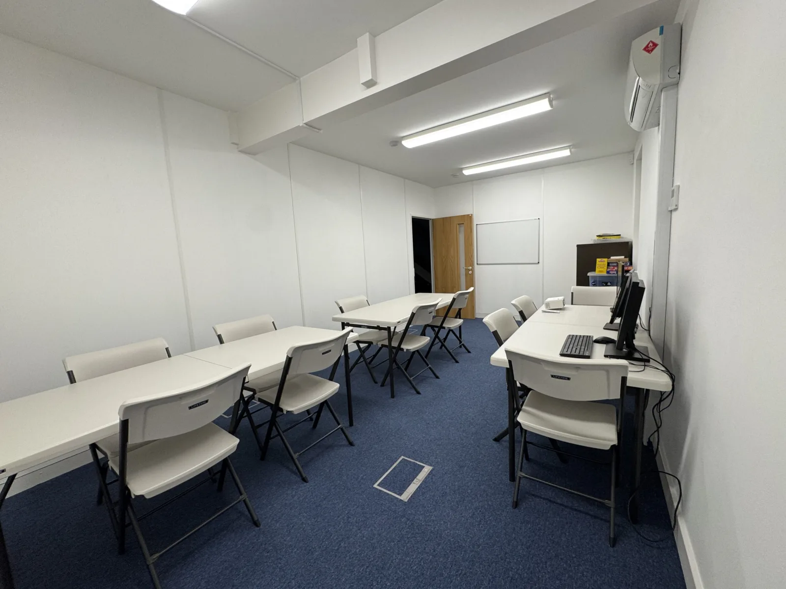A training room with folding tables arranged in rows, a whiteboard on the far wall and a desktop computer along the side.